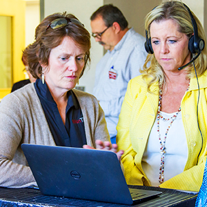 Two women, one with a headset, using a computer