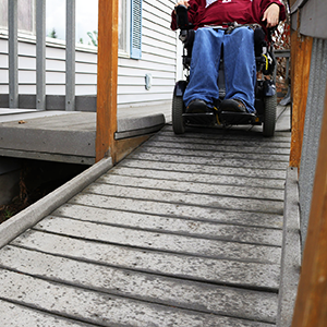 Bottom half of a person in a wheelchair about to go down a wooden ramp