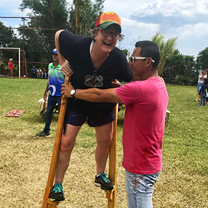 A woman stands on wooden stilts as a man supports her