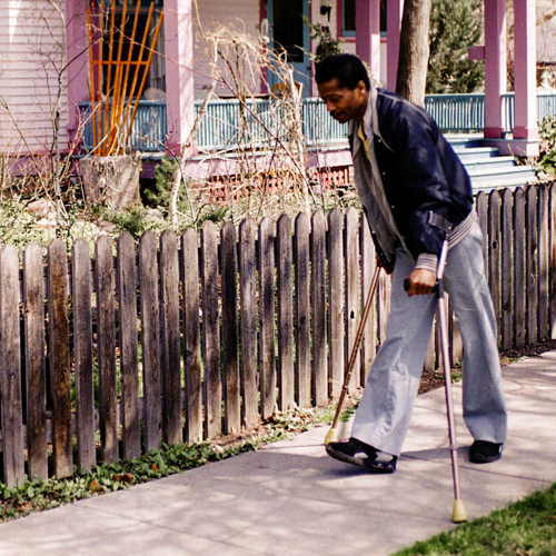 Man using crutches to walk down a sidewalk
