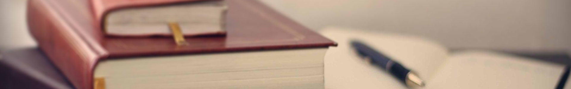 (Session Header Image): Two hardback books are closed next to an open composition notebook. A pen lays on a page of the open composition notebook.