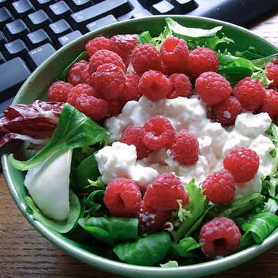 A salad with raspberries and cottage cheese with a computer keyboard in the background