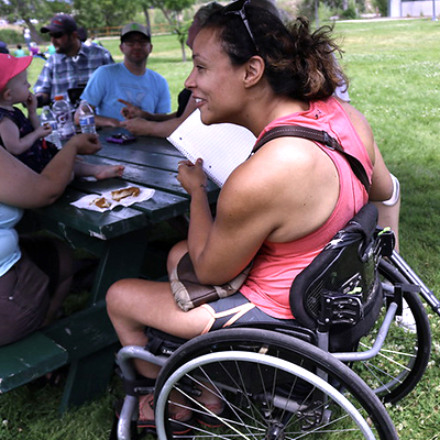 Woman in a wheelchair sitting at a picnic table with a group of people