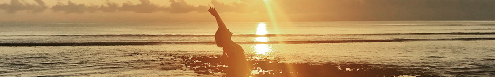 Silhouette of a woman in a yoga pose with a beach and sunset in the background